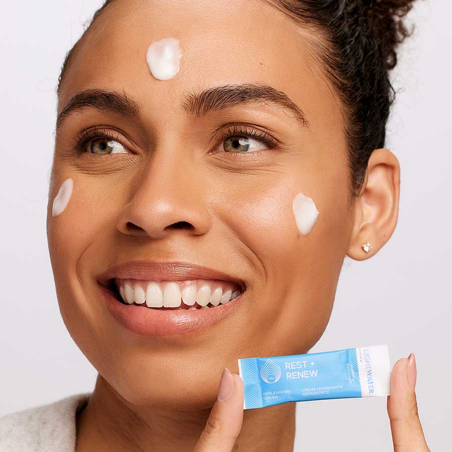 Woman holding LightWater PM Replenishing Cream daily dose and has cream on her face - LightWater Skin Nutrition is fresh from source to skin helping to nourish skin with fresh actives