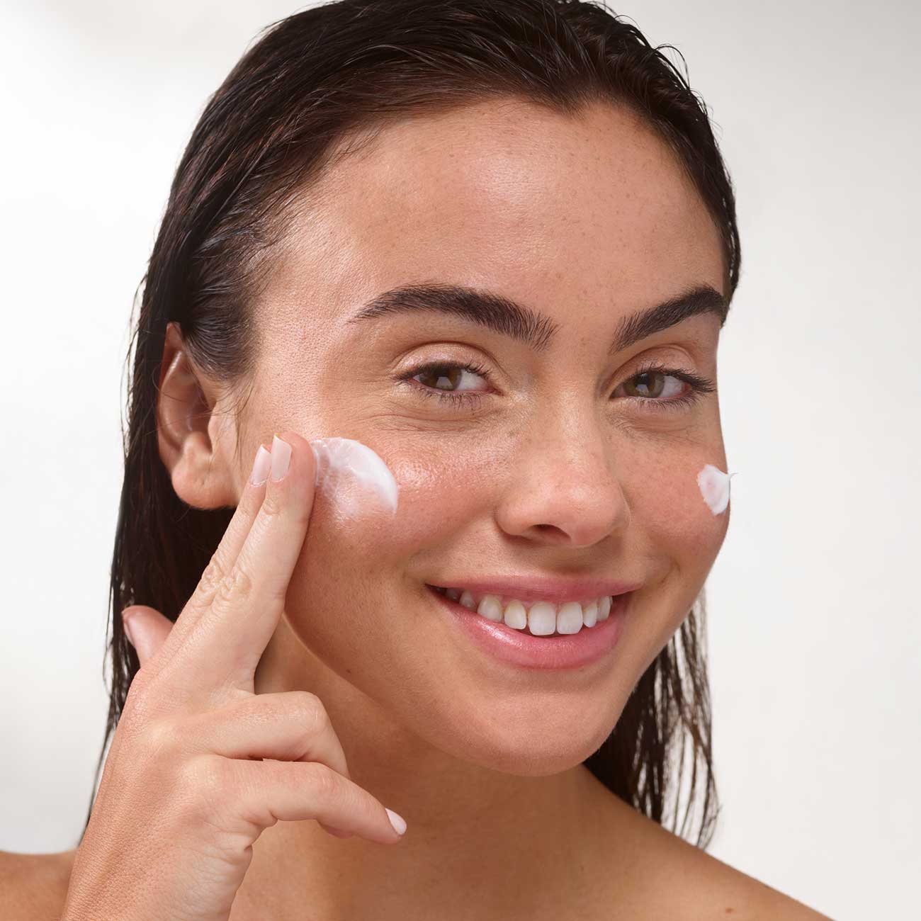 Woman happily applying daily dose of LightWater PM Replenishing Cream on face